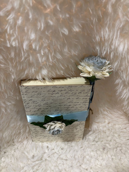 Notebook w/ pen featuring a soft close magnet in cream with writing and white and blue flowers with blue ribbons