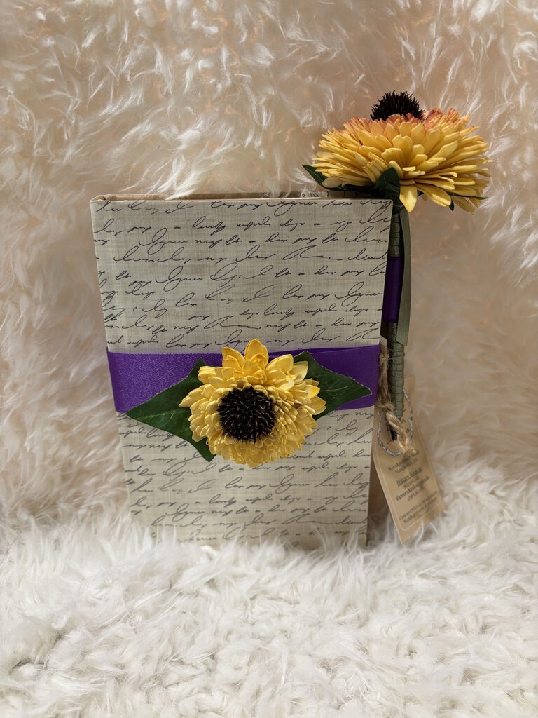 Notebook w/ pen featuring a soft close magnet in cream with writing and sunflowers with purple ribbon