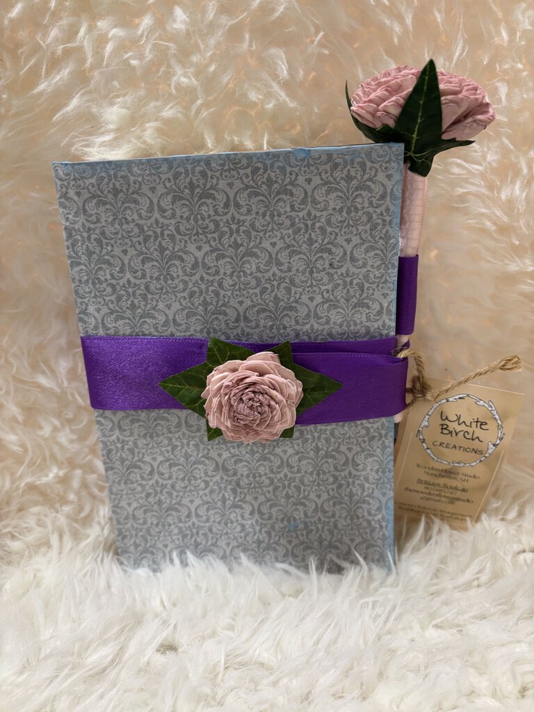 Notebook w/ pen featuring a soft close magnet in light blue pattern with blue paint accents, pink flowers and purple ribbon